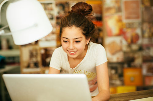 Teen girl doing schoolwork on computer in bedroom